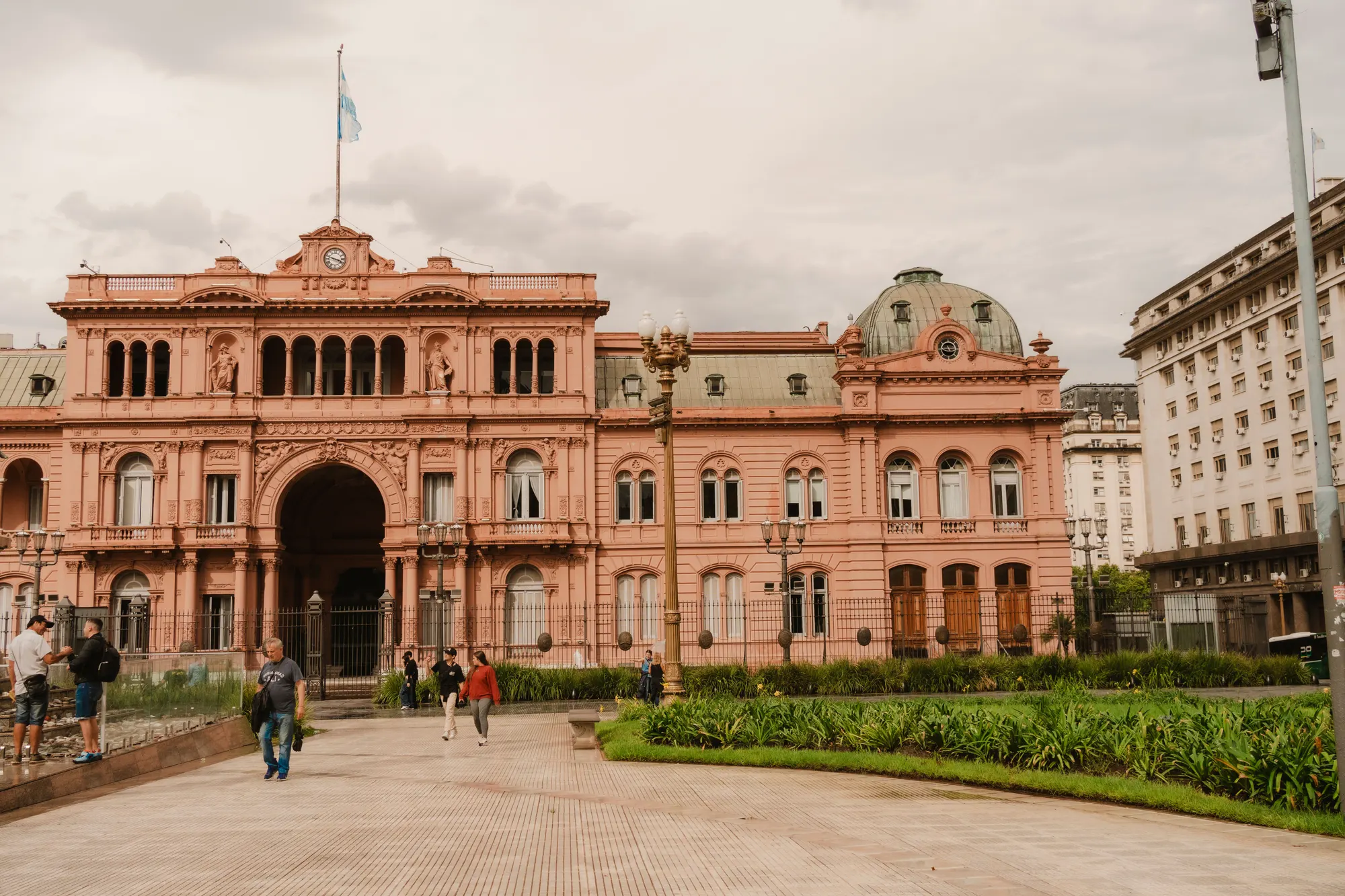 Fachada de la Casa Rosada, en Buenos Aires, con la bandera argentina y transeúntes en primer plano.